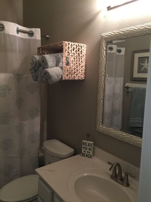 A bathroom with a toilet, sink, and shower curtain. There is a towel rack with folded towels and a sign that says "RELAX YOU'RE at the BEACH". - Best pool on the Island! Walk to beach! & 10/10 Rated! (Corpus Christi)
