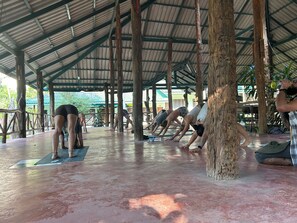A covered outdoor area with wooden beams and a metal roof, featuring a group of people doing yoga on mats. - Chill Out Bar and Bungalows (Krabi)