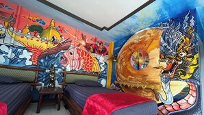 Een kamer met een muurschildering, een bed, een stoel en een klein tafeltje.