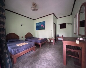 Une chambre avec deux lits, une table, une chaise, un miroir, un ventilateur et un tableau accroché au mur.