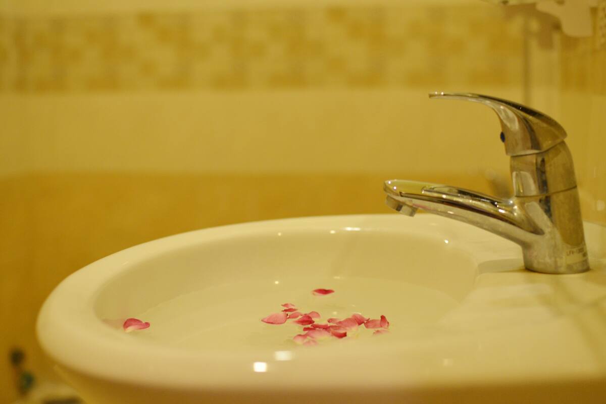 Uma pia de banheiro com uma torneira cromada e uma tigela com pétalas de rosa.