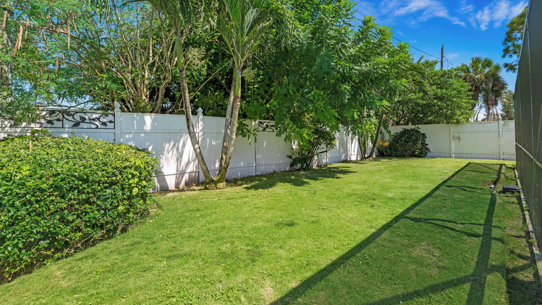 Un jardin bien entretenu avec une pelouse, une haie et une clôture blanche.