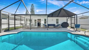Una piscina exterior techada con zona de patio, que incluye asientos y una parrilla cubierta.