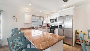 Una cocina moderna con armarios blancos, encimera de granito, electrodomésticos de acero inoxidable y sillas azules.