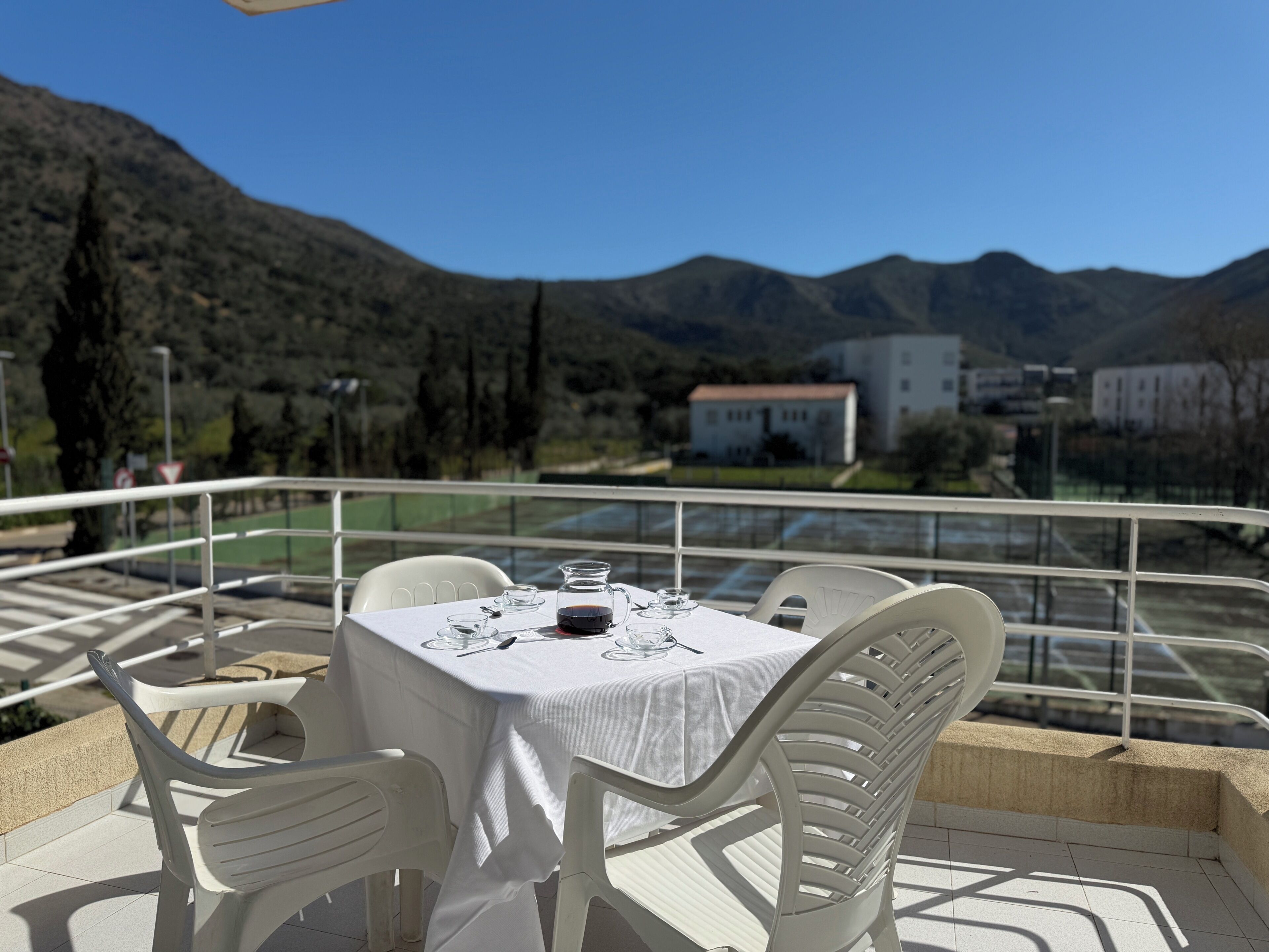 Mesa al aire libre con vistas a la montaña, sillas blancas y mantel.