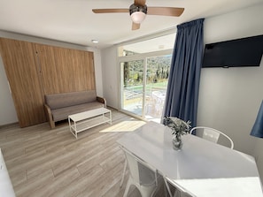 A modern room with a wooden wardrobe, a grey sofa, a white table, and a ceiling fan.