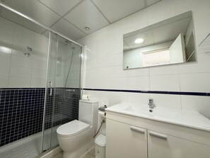 A bathroom with a glass-enclosed shower, a toilet, a sink, and a mirror.
