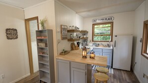 A compact kitchen with white cabinetry, a wooden countertop, and a 'Our Happy Place' sign. - The Bay Tiny House - Romantic Hideaway (Williams Bay)