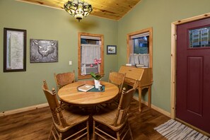 Un coin repas avec une table ronde en bois, quatre chaises, un lustre et des œuvres d’art encadrées accrochées aux murs.