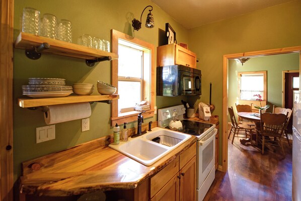 A kitchen with wooden countertops, a sink, a stove, and a microwave. There are shelves with dishes and a window above the sink. - Spectacular setting, amenities, and centrally located to Mt. Rushmore and Custer State Park, and hiking. Wi-Fi. Excellent cell service (Verizon & ATT). Private campfire. Off-season discounts. No extra fees. (Rapid City)