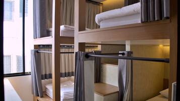 A hotel room with bunk beds, a window with curtains, and a wooden desk.