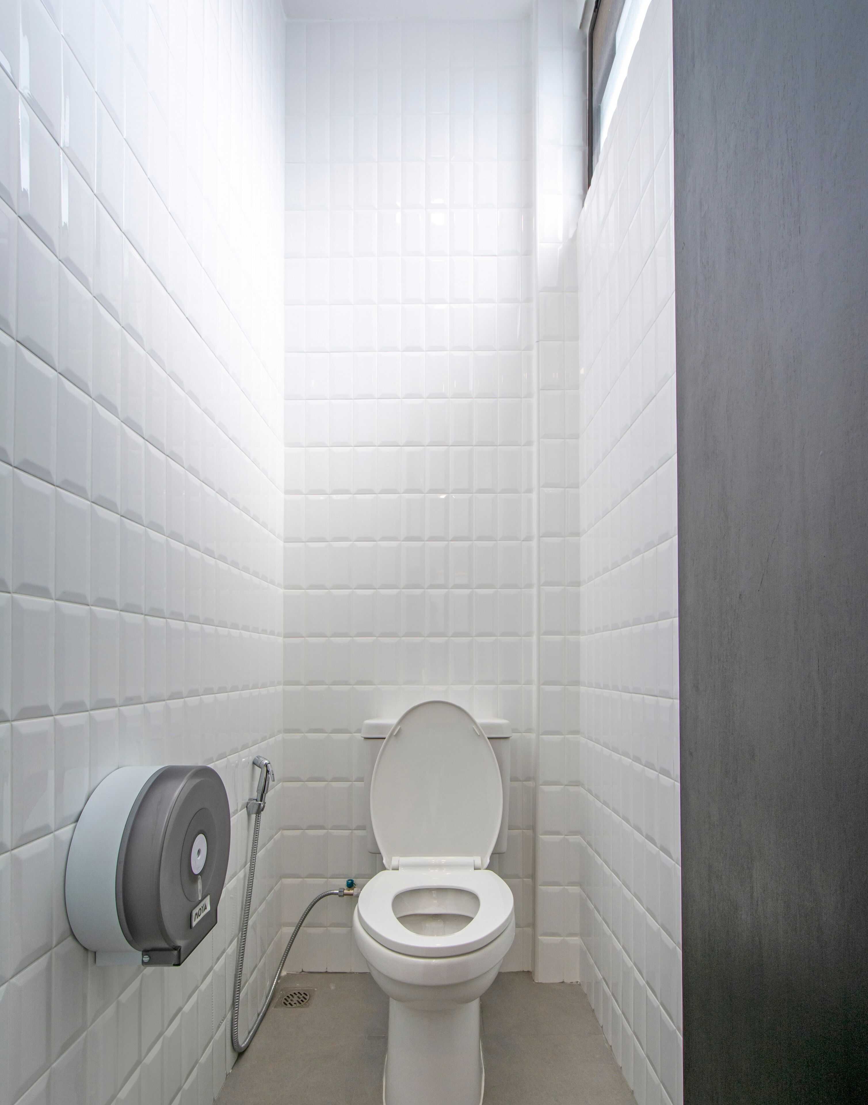 A small, modern bathroom with white tiles, a toilet, and a hand dryer.