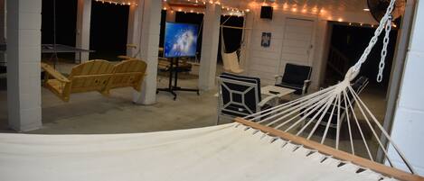 A hammock, two chairs, a desk, a TV, and string lights in a room with white walls and ceiling.