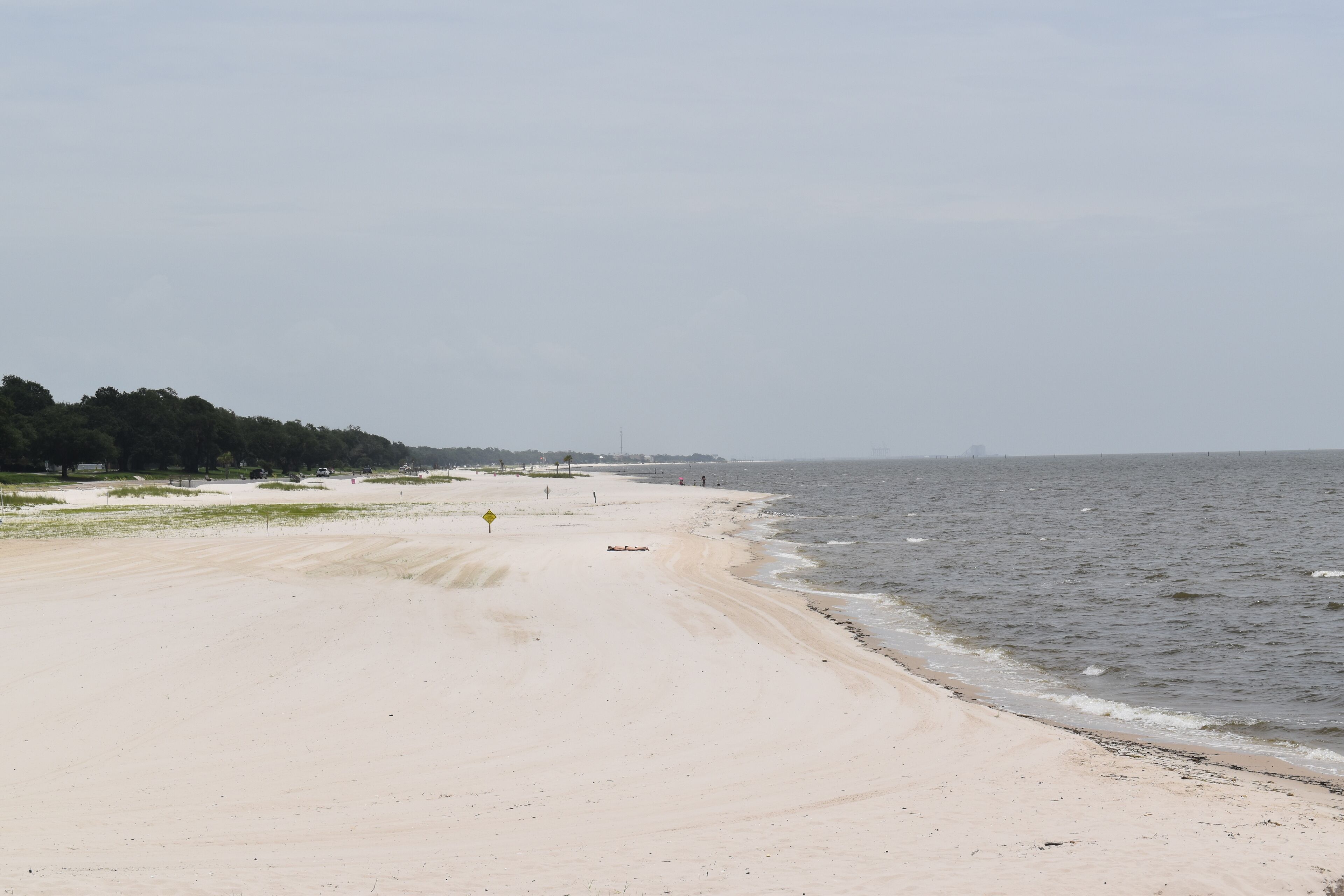 A beach with a sandy shore, a few people in the distance, and a clear sky.