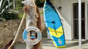 A lifebuoy with "WELCOME ONBOARD" and a mascot, a surfboard, and a stone wall in the background.