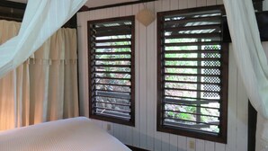 A room with a bed, two windows with wooden shutters, and a ceiling fan. - Water Front Casita w pool On Tropical One Acre Estate (Roatan)