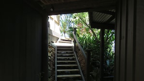 A wooden staircase leading to a covered outdoor area with a view of greenery and a building in the background. - Water Front Casita w pool On Tropical One Acre Estate (Roatan)
