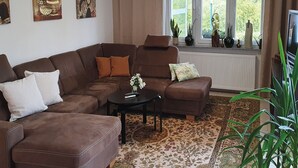 A living room with a brown leather sofa, a coffee table, and a large window with curtains. There are decorative vases on the windowsill and a plant in the corner. - Elisa Apartment Noswendel am See (Noswendel am See)