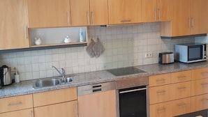 A modern kitchen with wooden cabinets, a stainless steel sink, a built-in oven, and a microwave. - Elisa Apartment Noswendel am See (Noswendel am See)