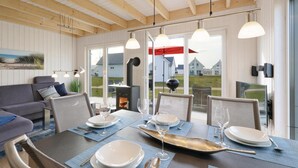 Un comedor con una mesa dispuesta para cuatro personas, un sofá y vistas a casas a través de grandes ventanales.