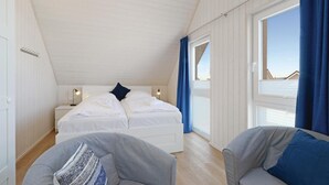 Un dormitorio con cama, dos lámparas de noche, ventana con cortinas y vista al mar.