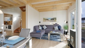 Una sala de estar moderna con un sofá, una mesa de centro y un comedor con una mesa dispuesta para dos personas.