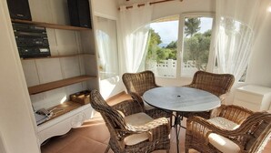 A sunlit patio with wicker furniture, a round table, and a built-in shelf with electronic devices.