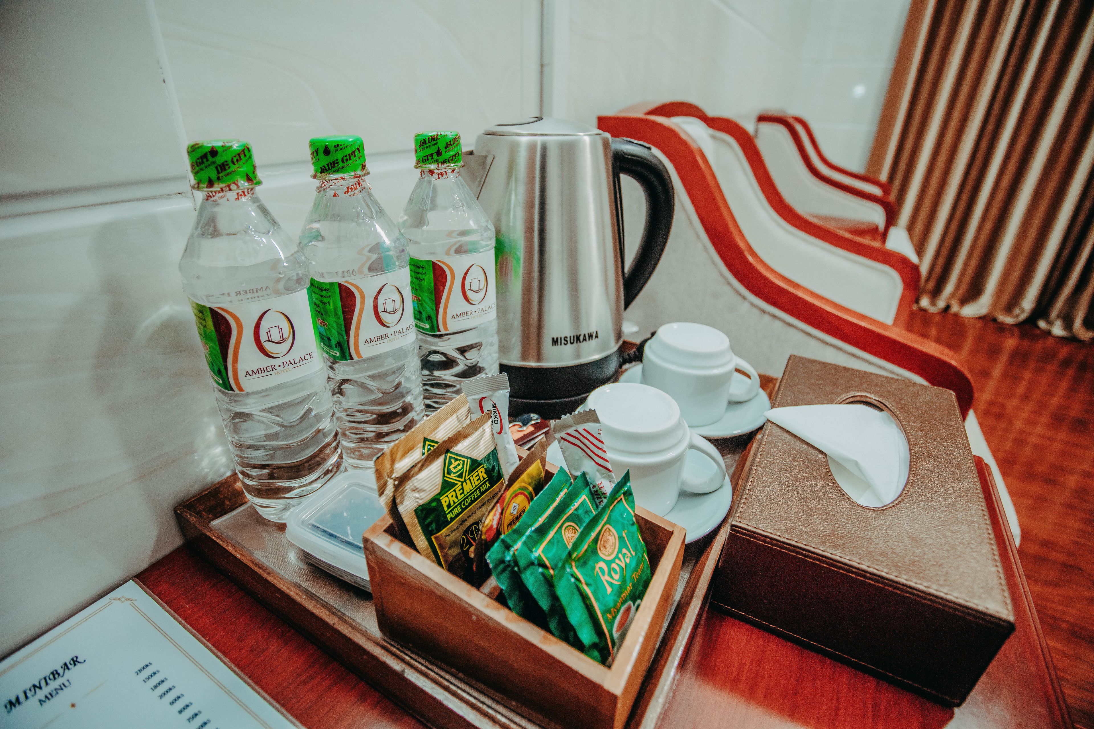 A tray with bottled water, coffee packets, a coffee pot, cups, and a tissue box on a wooden tray in a hotel room.