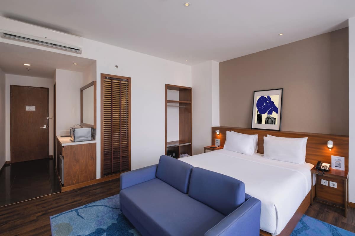 Ein Hotelzimmer mit einem großen Bett, einem blauen Sofa, einem Holzschrank, einem Spiegel und einem gerahmten Kunstwerk an der Wand.