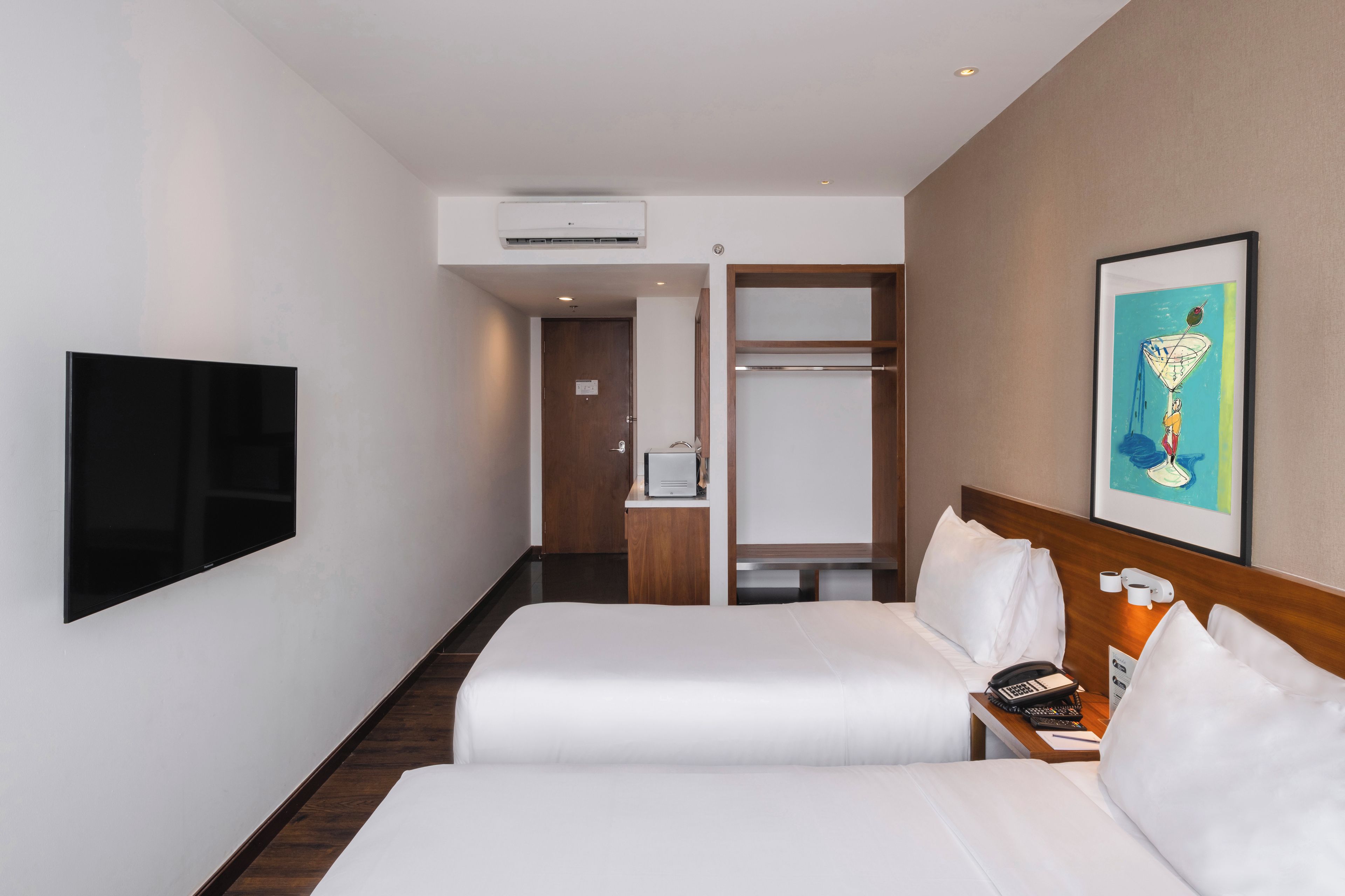 A hotel room with two beds, a TV, a painting, and a desk with a phone.