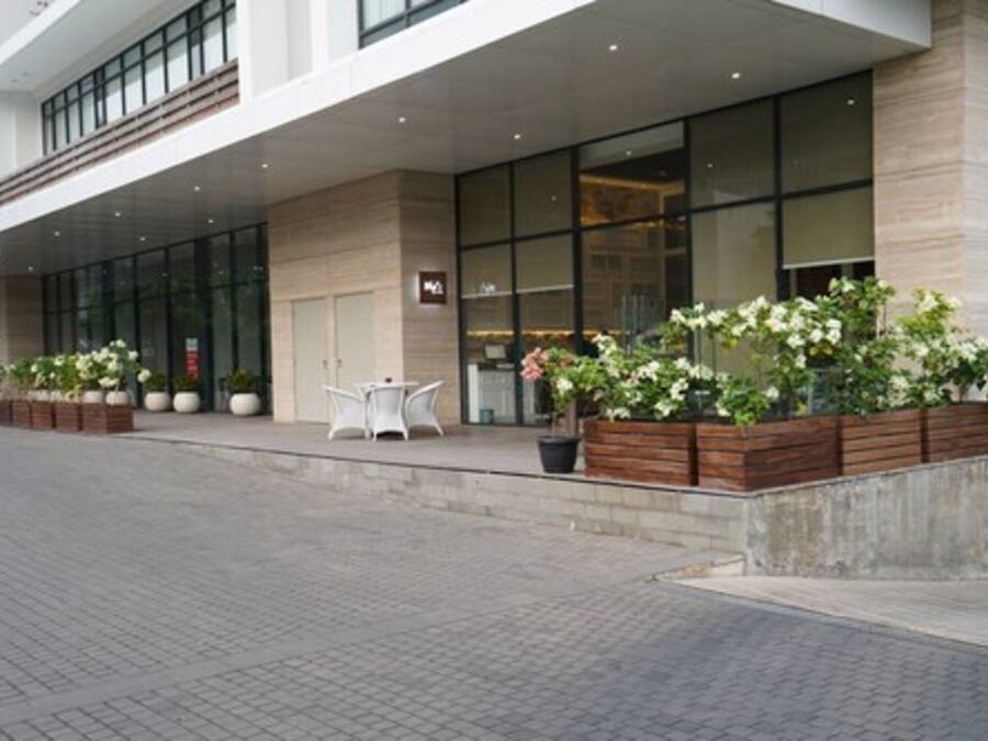 A modern hotel entrance with large glass windows, outdoor seating, and potted plants.