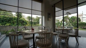 A modern indoor dining area with large windows, wooden furniture, and a view of greenery outside. - Veranda Serviced Residence Puri (Jakarta)