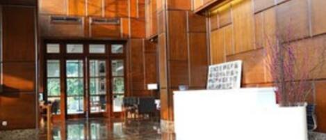 A spacious lobby with a polished stone floor, wooden paneling on the walls, and a reception desk.