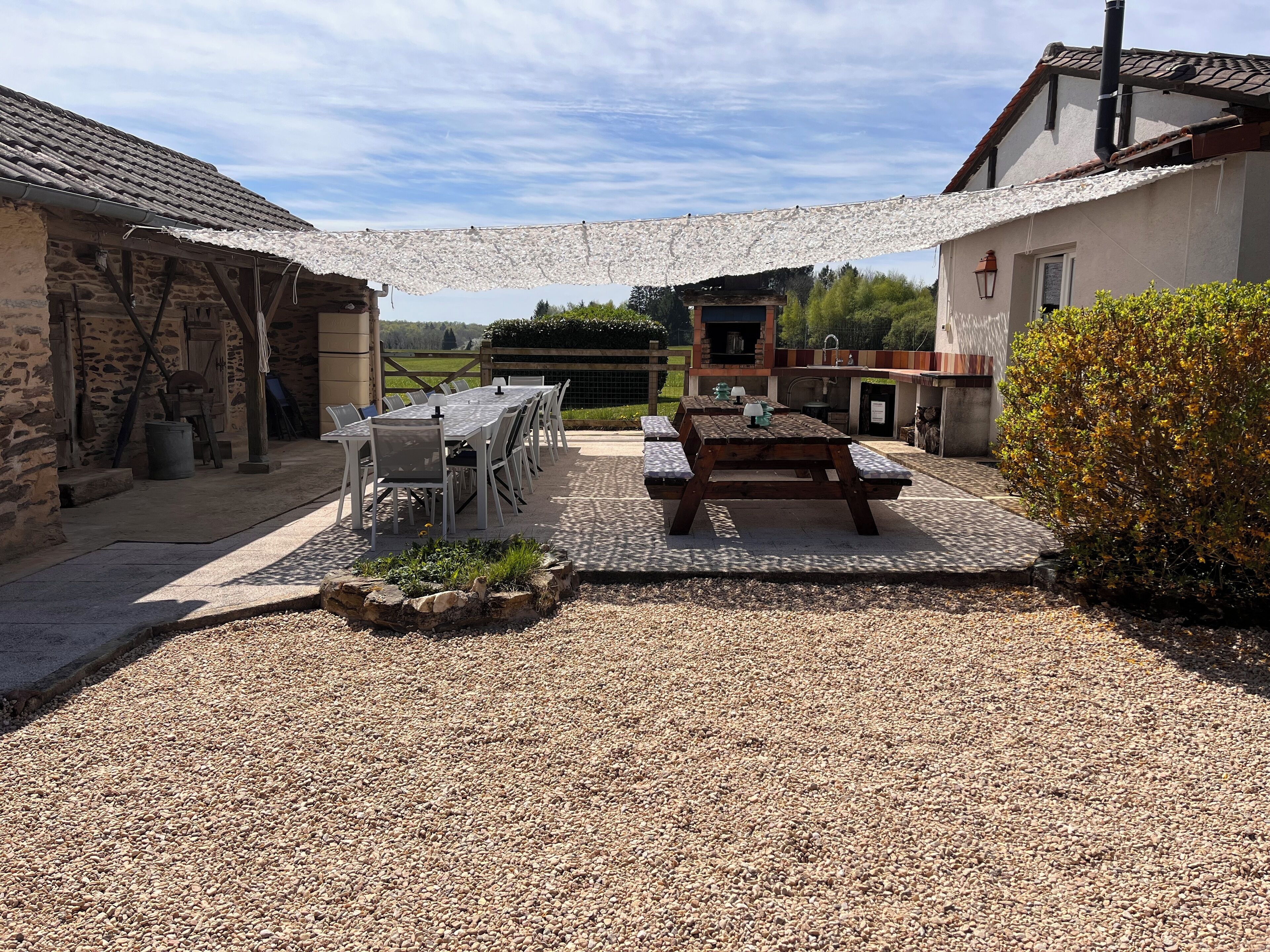 A rustic outdoor dining area with a stone table and benches, surrounded by stone walls and a gravel ground.