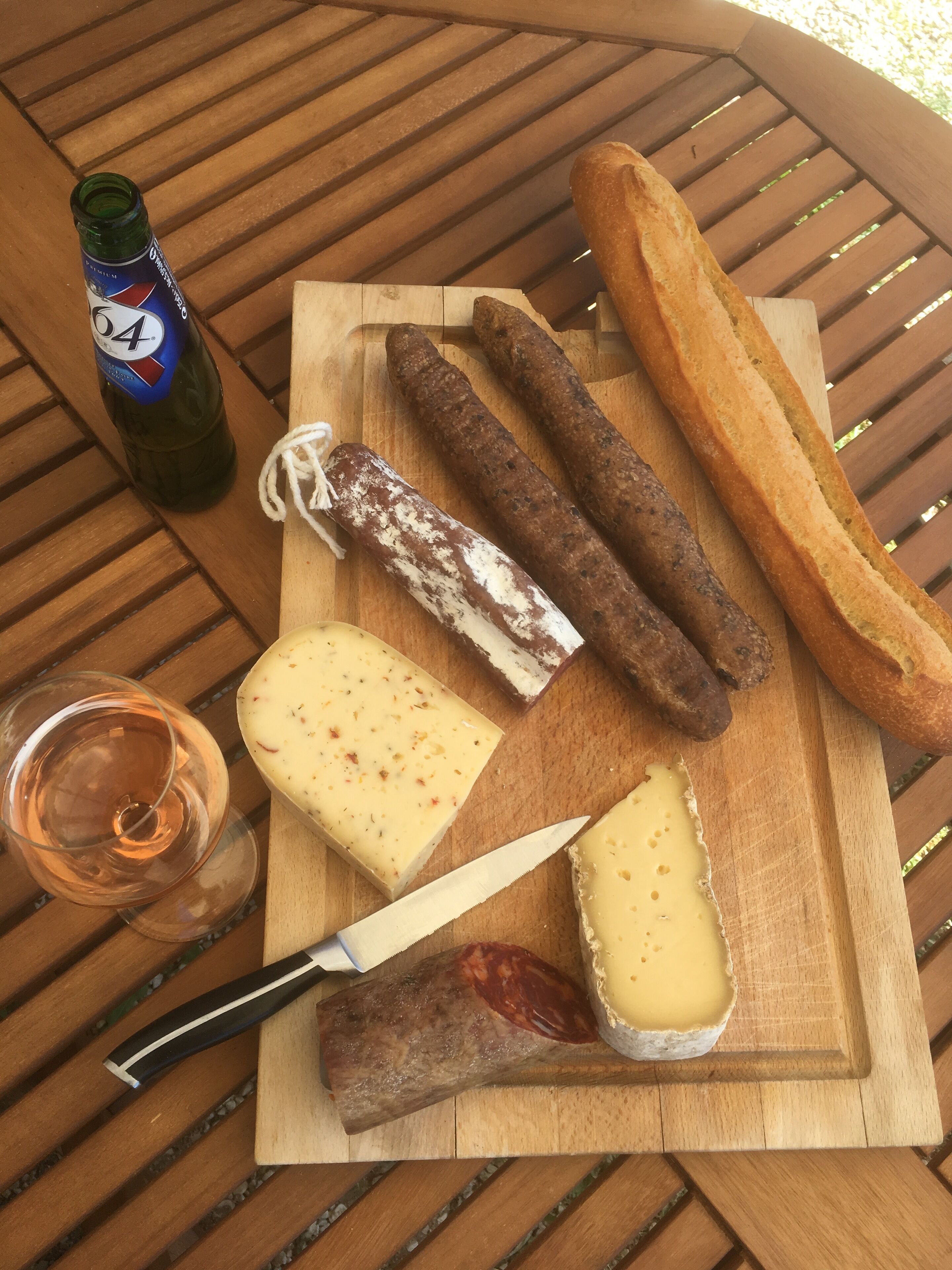 A wooden cutting board with various cheeses, cured meats, and a baguette on a table.
