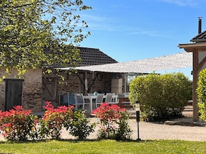 A stone building with a covered outdoor seating area, surrounded by greenery and a clear sky. - Studio in the old hayloft (Chalais)