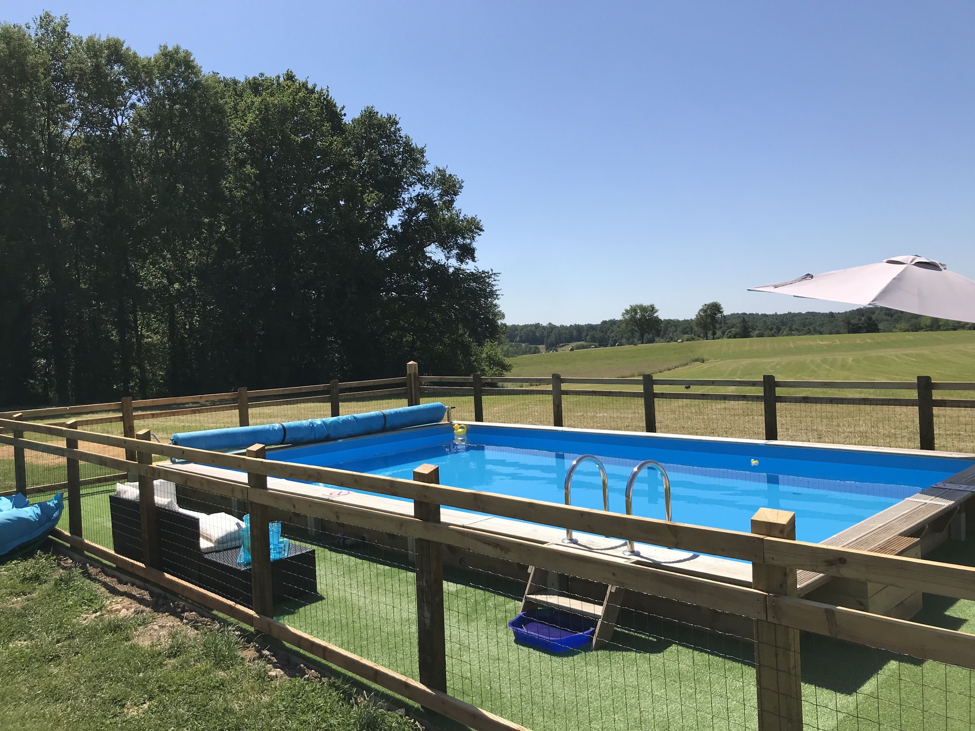 Una piscina rectangular con un muelle de madera y una valla.