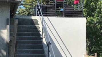Un escalier menant à un balcon agrémenté d’un parasol coloré, d’un banc en bois et d’une clôture.