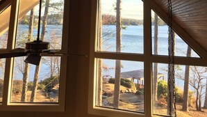 Una habitación con techo inclinado y ventanas amplias que dan vistas a un lago y árboles.