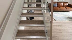 Eine moderne Treppe mit Glasgeländern führt zu einem Wohnbereich mit einem braunen Ledersofa und abstrakten Wandbildern.