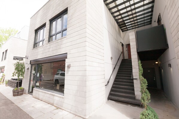 A modern building with a large glass storefront, a staircase leading to an upper level, and a small tree planted outside.