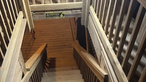 Una escalera de madera con un letrero de precaución, barandales de madera y advertencia de cuidado con la cabeza.