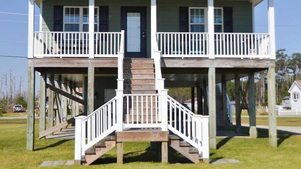 Ein zweistöckiges Haus mit einer Veranda, einer zentralen Treppe und einem kleinen Deck im oberen Geschoss.