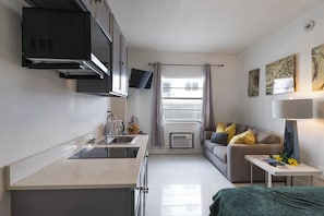 Un espacio habitable compacto con kitchenette, un sofá, una mesita y obras de arte en las paredes.