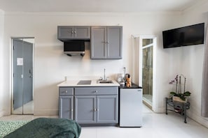 Una cocina compacta con armarios grises, un refrigerador pequeño, un lavamanos y un televisor montado en la pared.
