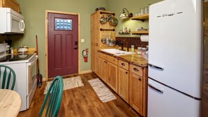 A compact kitchen with a red door, wooden cabinets, a white refrigerator, and a small dining area with a table and chairs. - Spectacular setting, amenities, and centrally located to Mt. Rushmore and Custer State Park, and hiking. Wi-Fi. Excellent cell service (Verizon & ATT).A favorite cabin for honeymoons and anniversaries Private campfire. Off-season discounts. No extra (Rapid City)