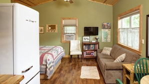 A cozy room with a bed, a sofa, a chair, a small table, a bookshelf, a ceiling fan, and a window with curtains. - Spectacular setting, amenities, and centrally located to Mt. Rushmore and Custer State Park, and hiking. Wi-Fi. Excellent cell service (Verizon & ATT).A favorite cabin for honeymoons and anniversaries Private campfire. Off-season discounts. No extra (Rapid City)