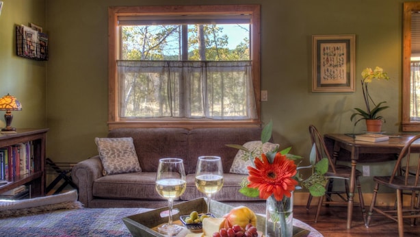 A cozy living room with a sofa, a dining table, and a window with a view of trees. - Spectacular setting, amenities, and centrally located to Mt. Rushmore and Custer State Park, and hiking. Wi-Fi. Excellent cell service (Verizon & ATT).A favorite cabin for honeymoons and anniversaries Private campfire. Off-season discounts. No extra (Rapid City)