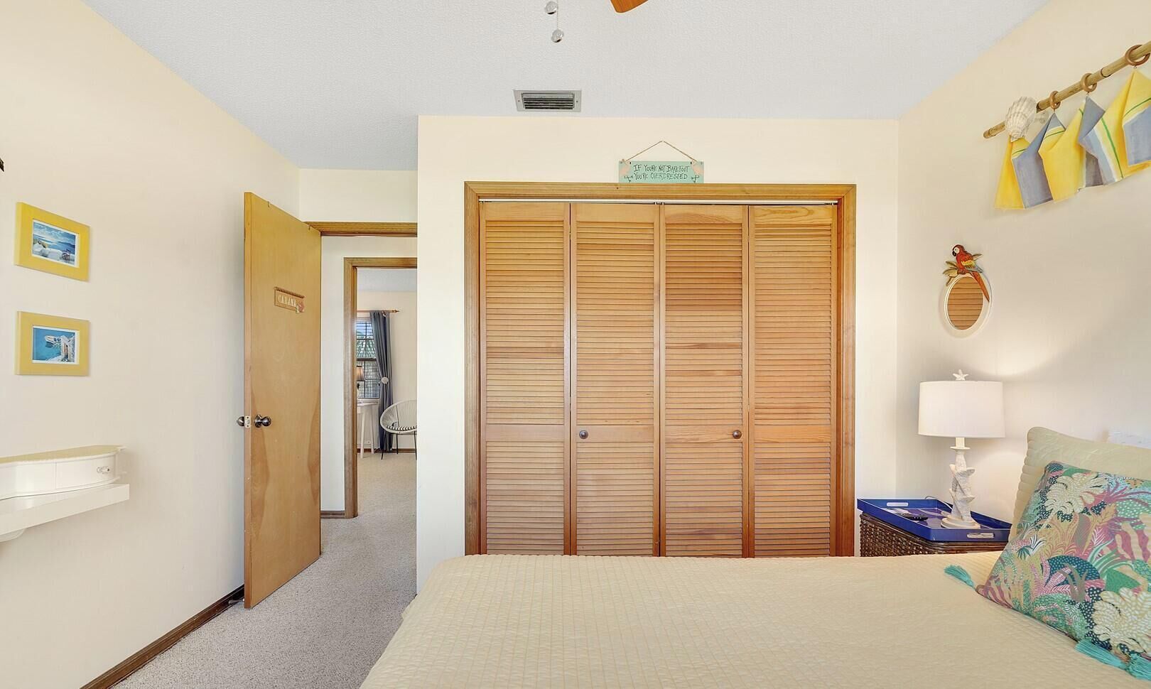 A bedroom with a bed, a wooden wardrobe, a bedside table with a lamp, and a chair in the background.