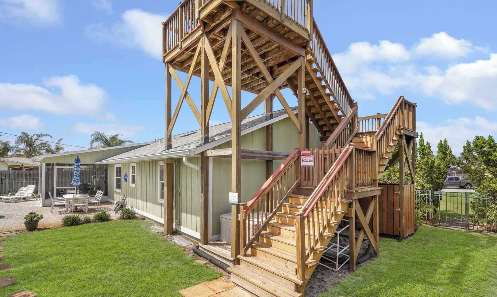 A two-story building with a wooden staircase and deck, a covered patio area, and a fenced yard.